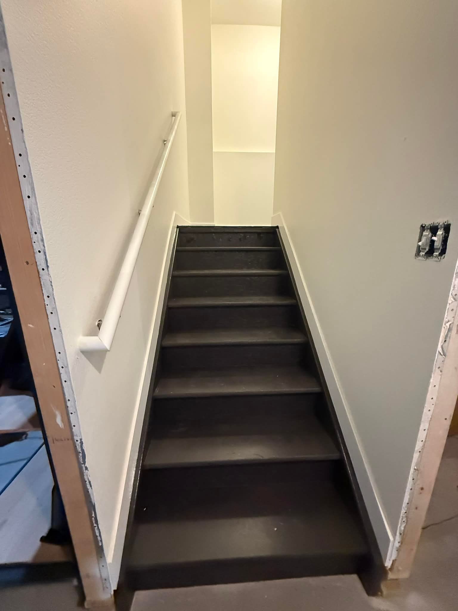 Narrow indoor stairway with dark steps, white walls, and a handrail on the left
