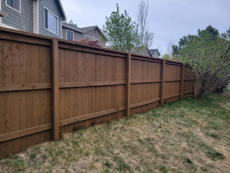 Wooden privacy fence along a grassy backyard beside a house and trees under a cloudy sky