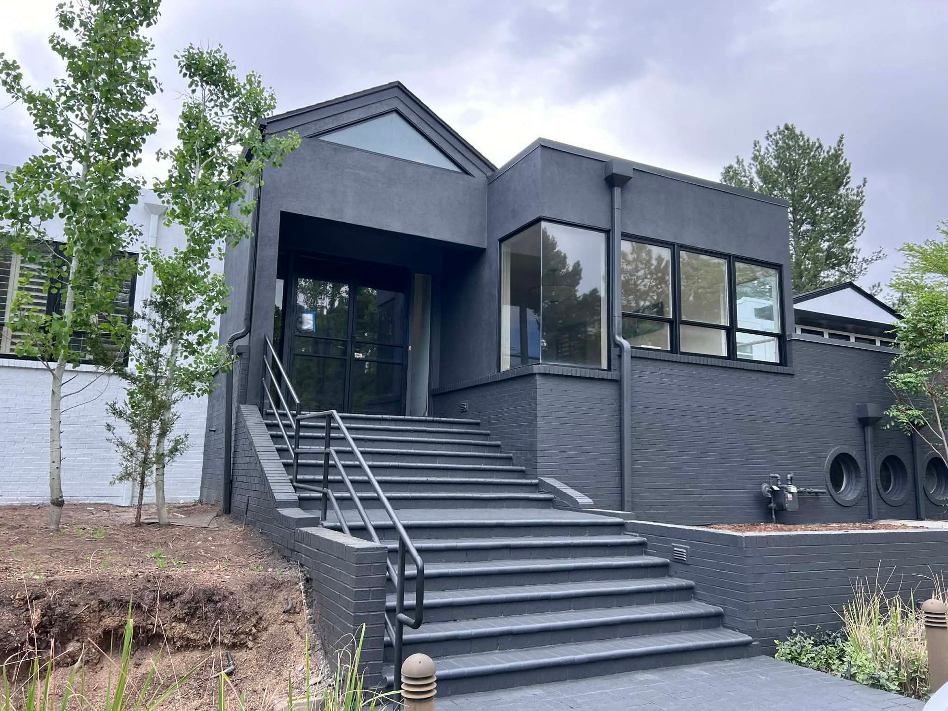 Modern gray brick house with a wide staircase, large windows, and a covered front entrance