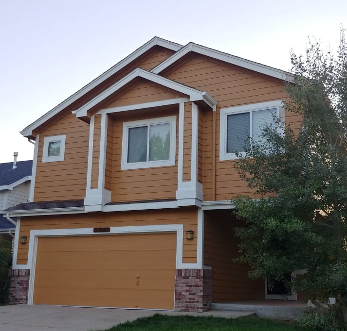 Two-story tan house with white trim, orange garage door, and brick accents