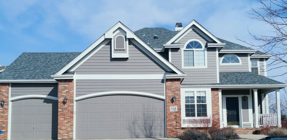 Suburban two-story gray house with brick accents, double garage, and front porch