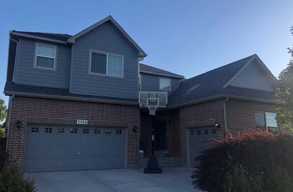 Two-story suburban house with a brick first floor, gray siding, garage, and basketball hoop in the driveway
