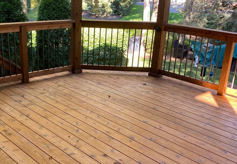 Wooden deck with brown railing overlooking a green backyard and trees