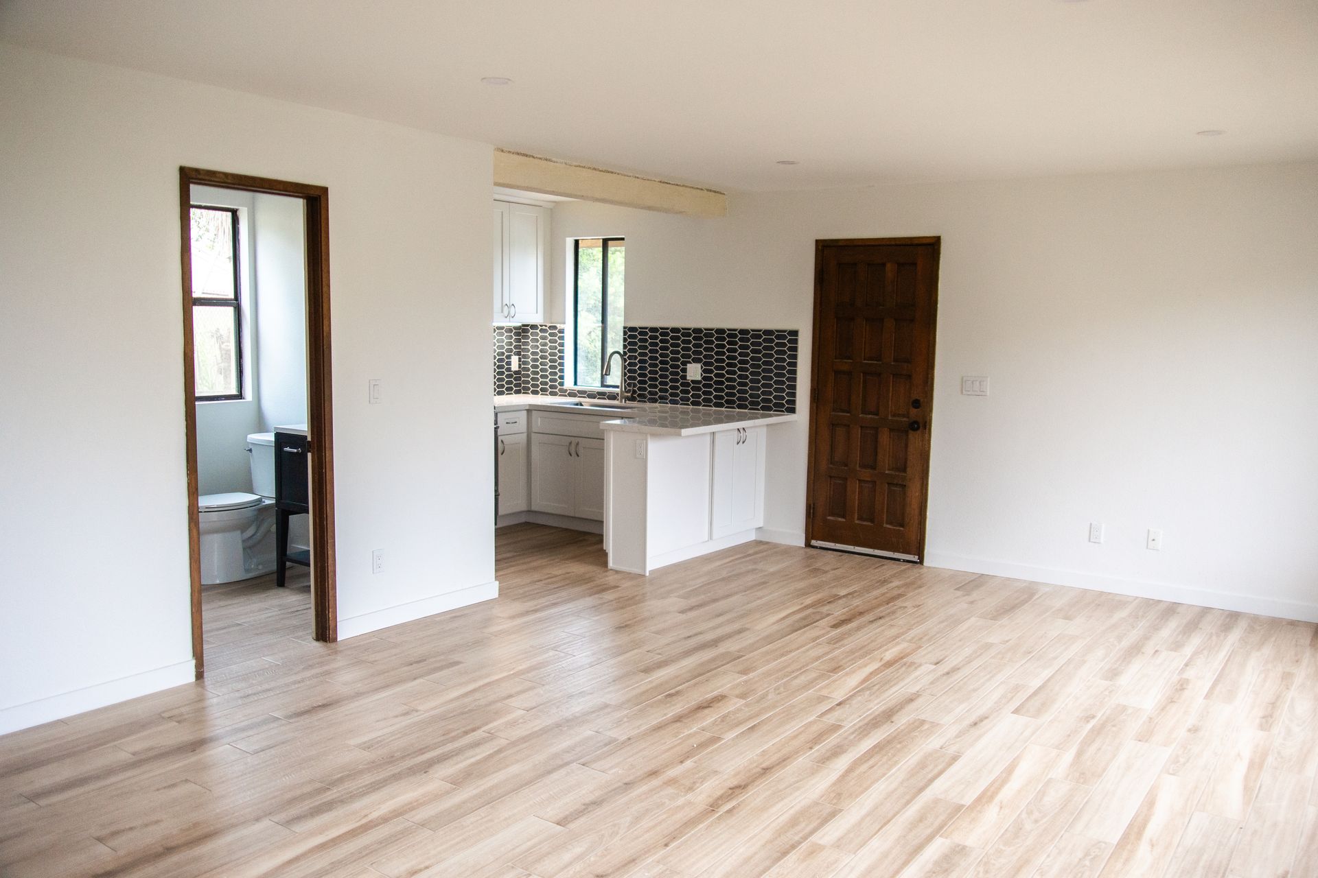 A remodeled ADU living room with hardwood floors and a kitchen in the background.