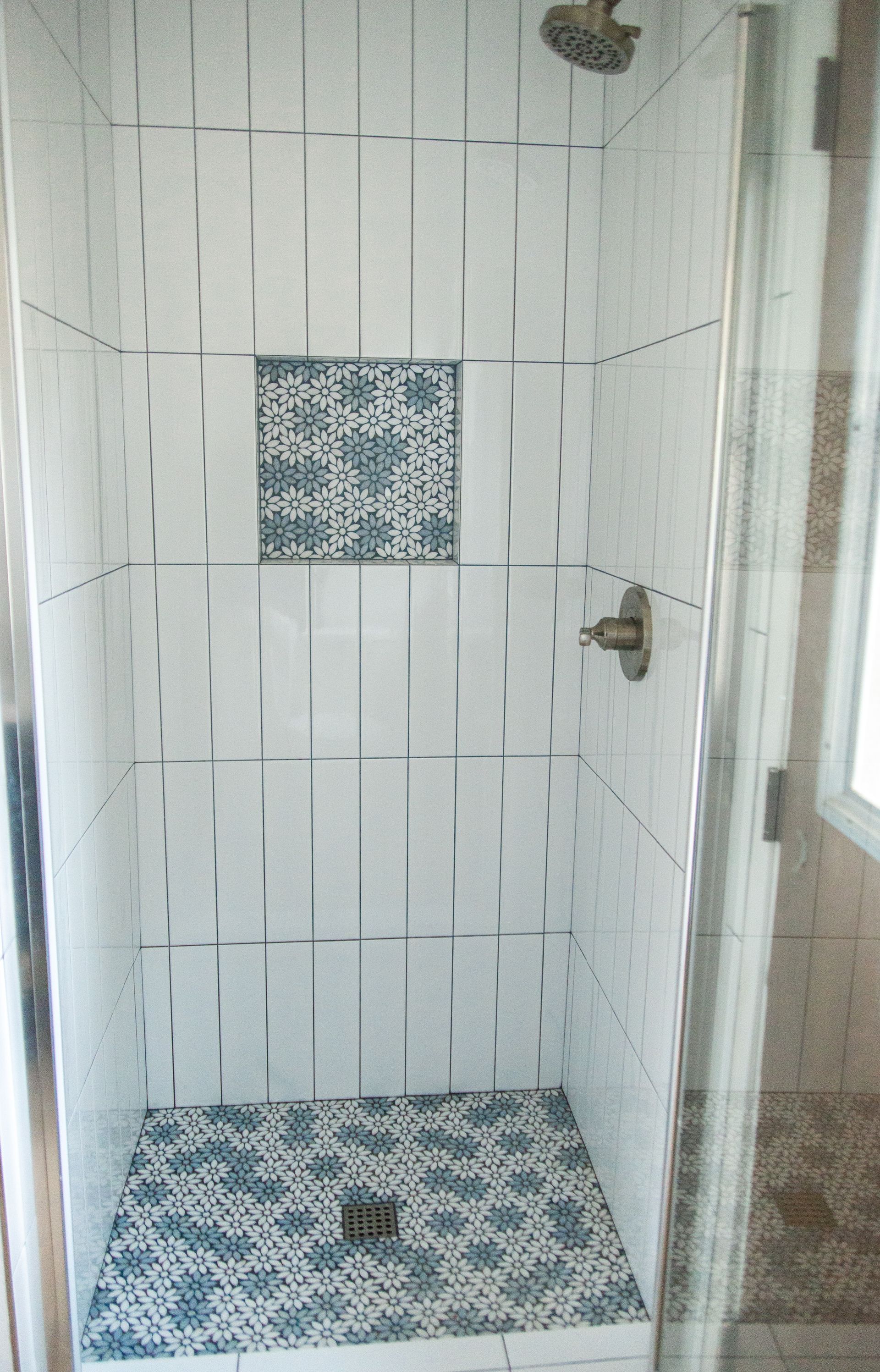 A remodeled ADU shower stall with white tiles and a blue tile niche.