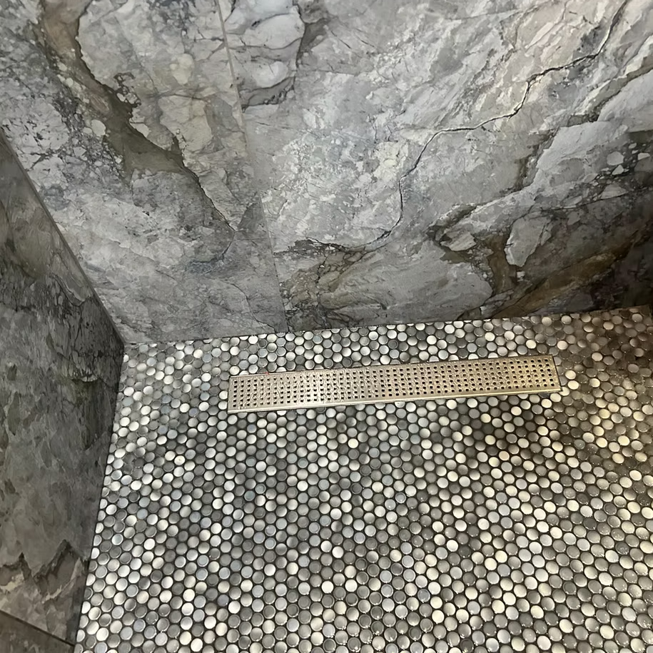 A shower with a drain on the floor and a marble wall.
