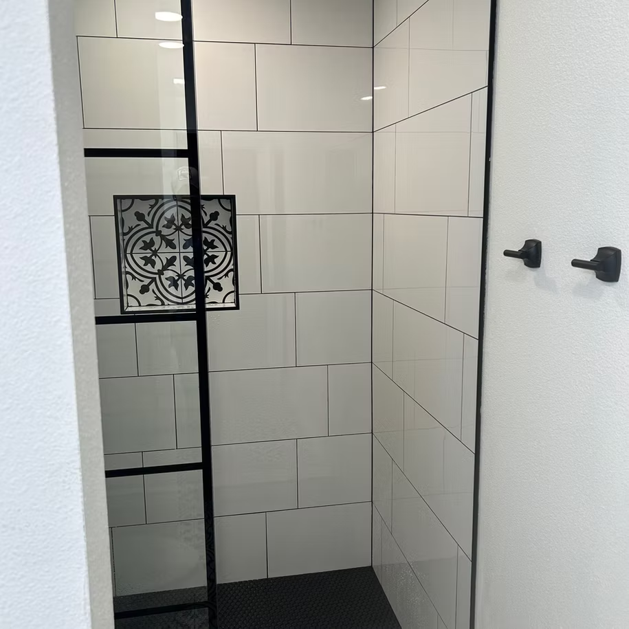 A remodeled shower with white tiles and a black frame.