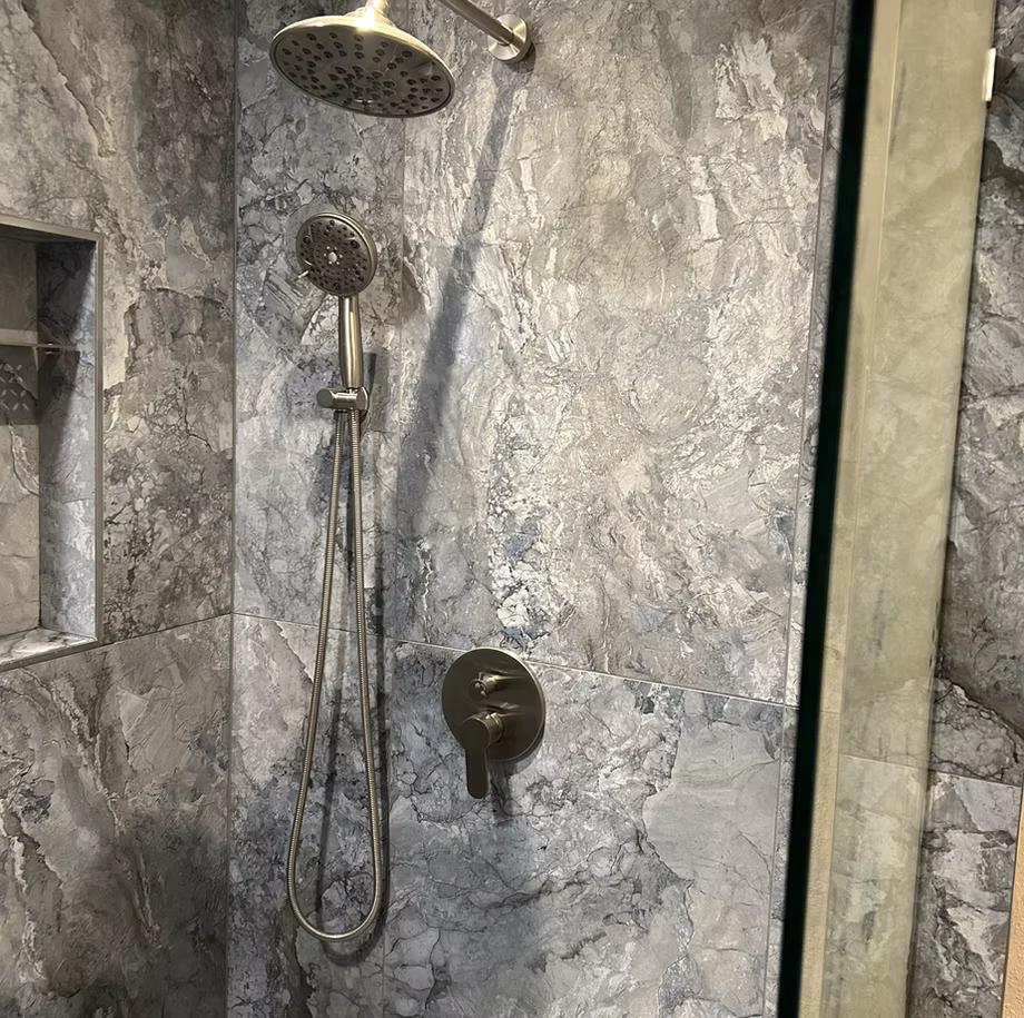 A remodeled shower with a marble wall and a shower head