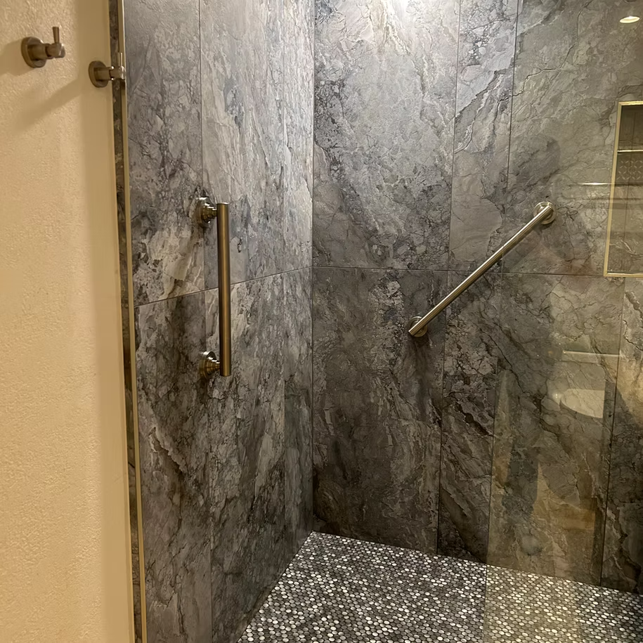 A bathroom with a walk in shower with a glass door and a marble wall.