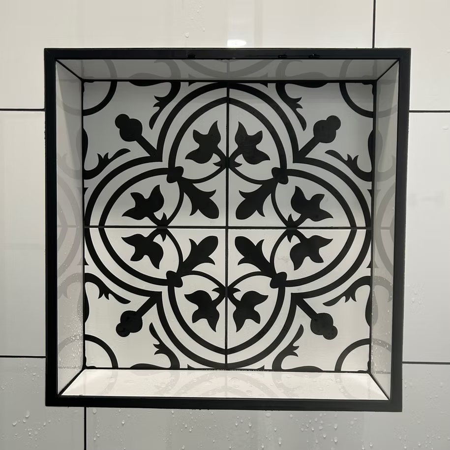 A black and white tile with a floral pattern is in a niche in a remodeled shower wall.