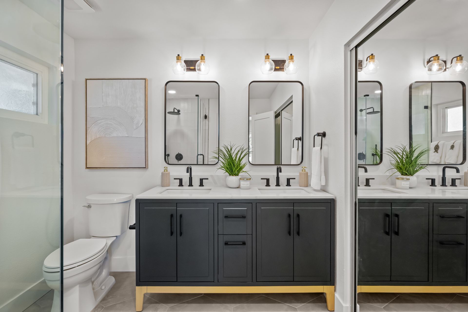 Bathroom with dual vanity, black cabinets, gold accents, and large mirrors.