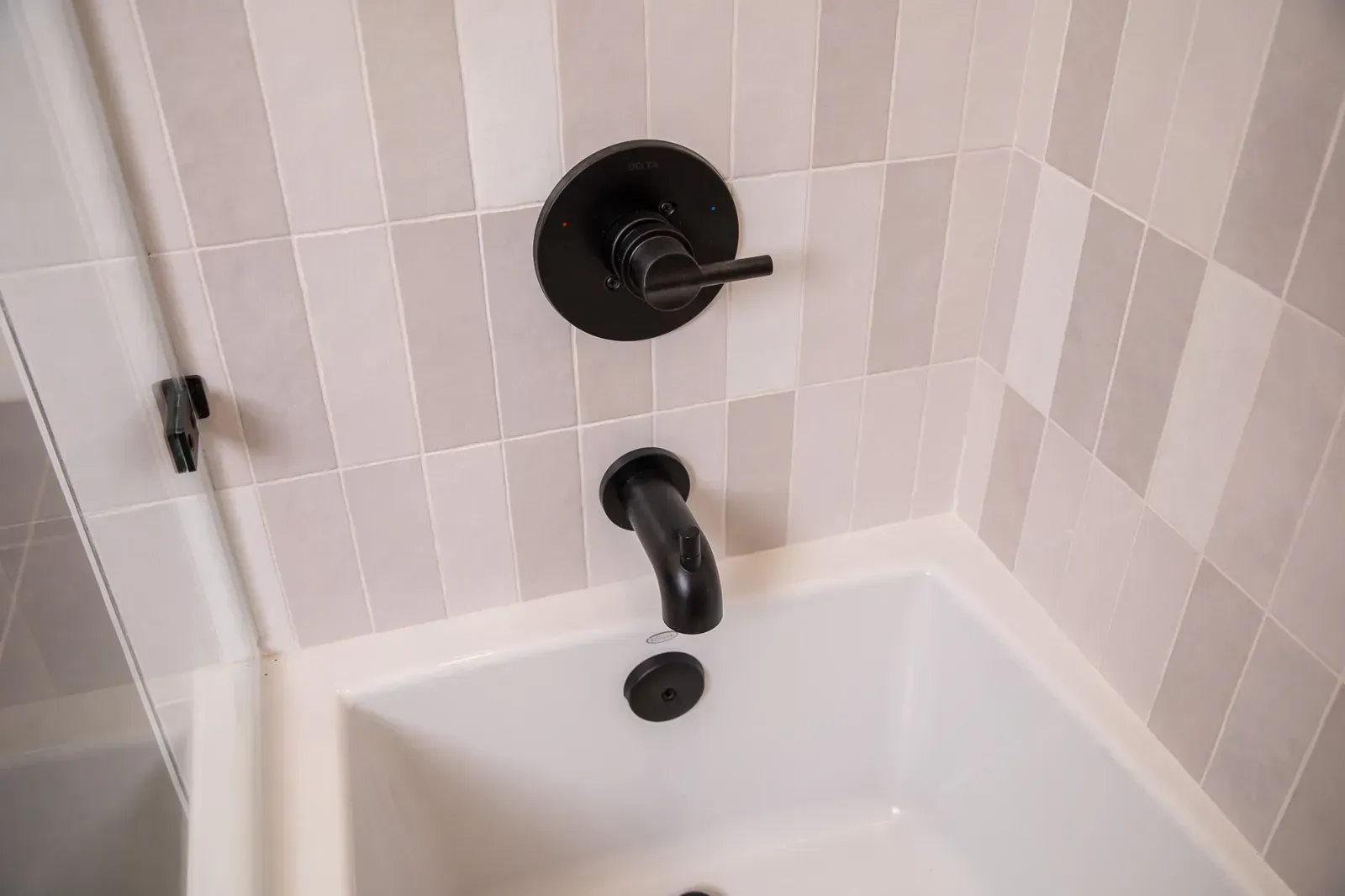 White bathtub corner with black faucet and shower trim against beige tiled walls