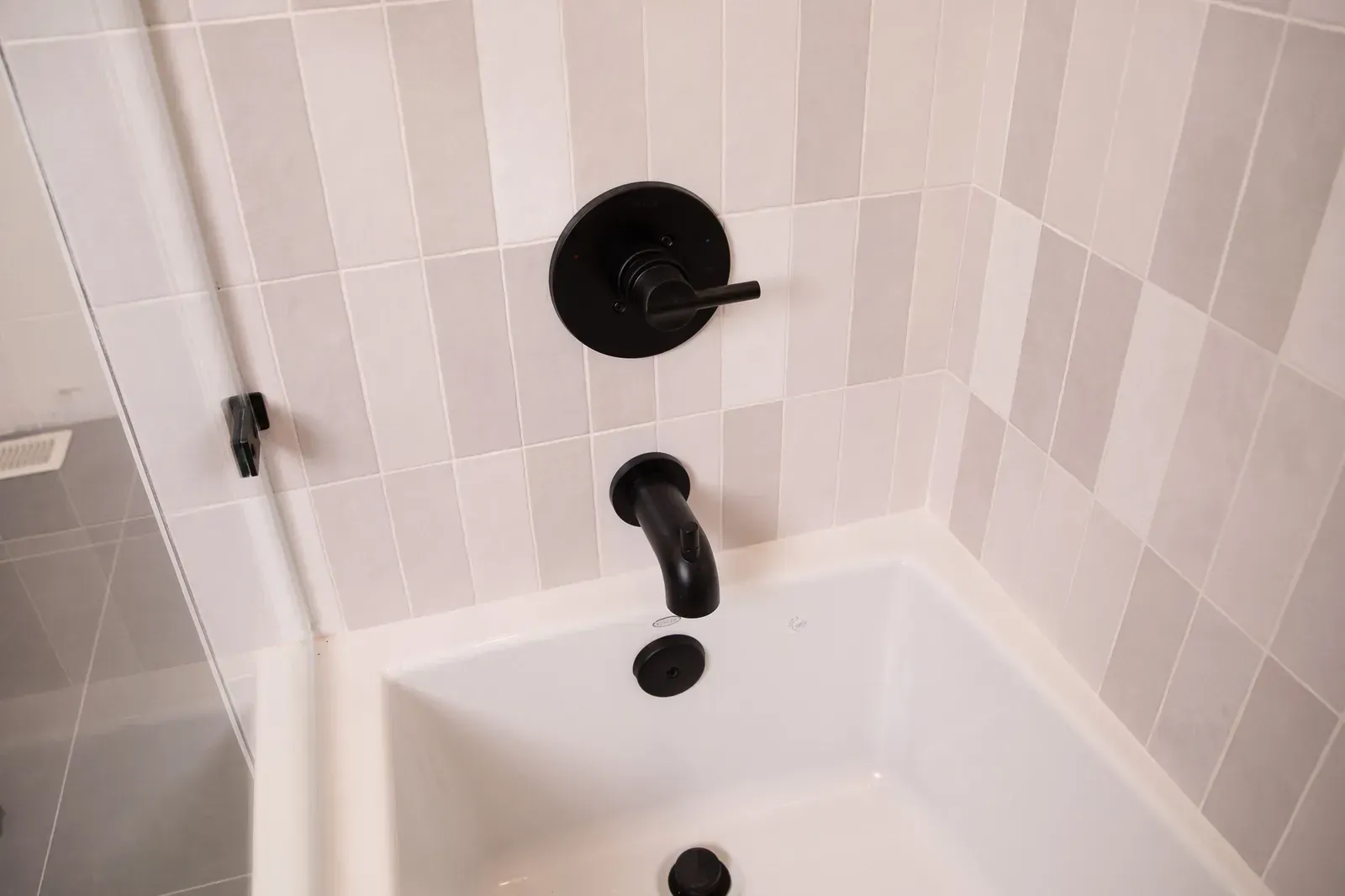 White bathtub with black faucet and drain in a tiled bathroom corner