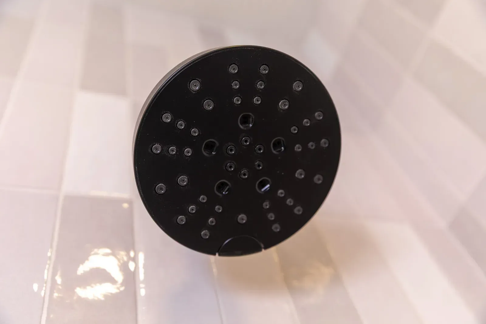 Black showerhead with many nozzles against white tiled shower wall