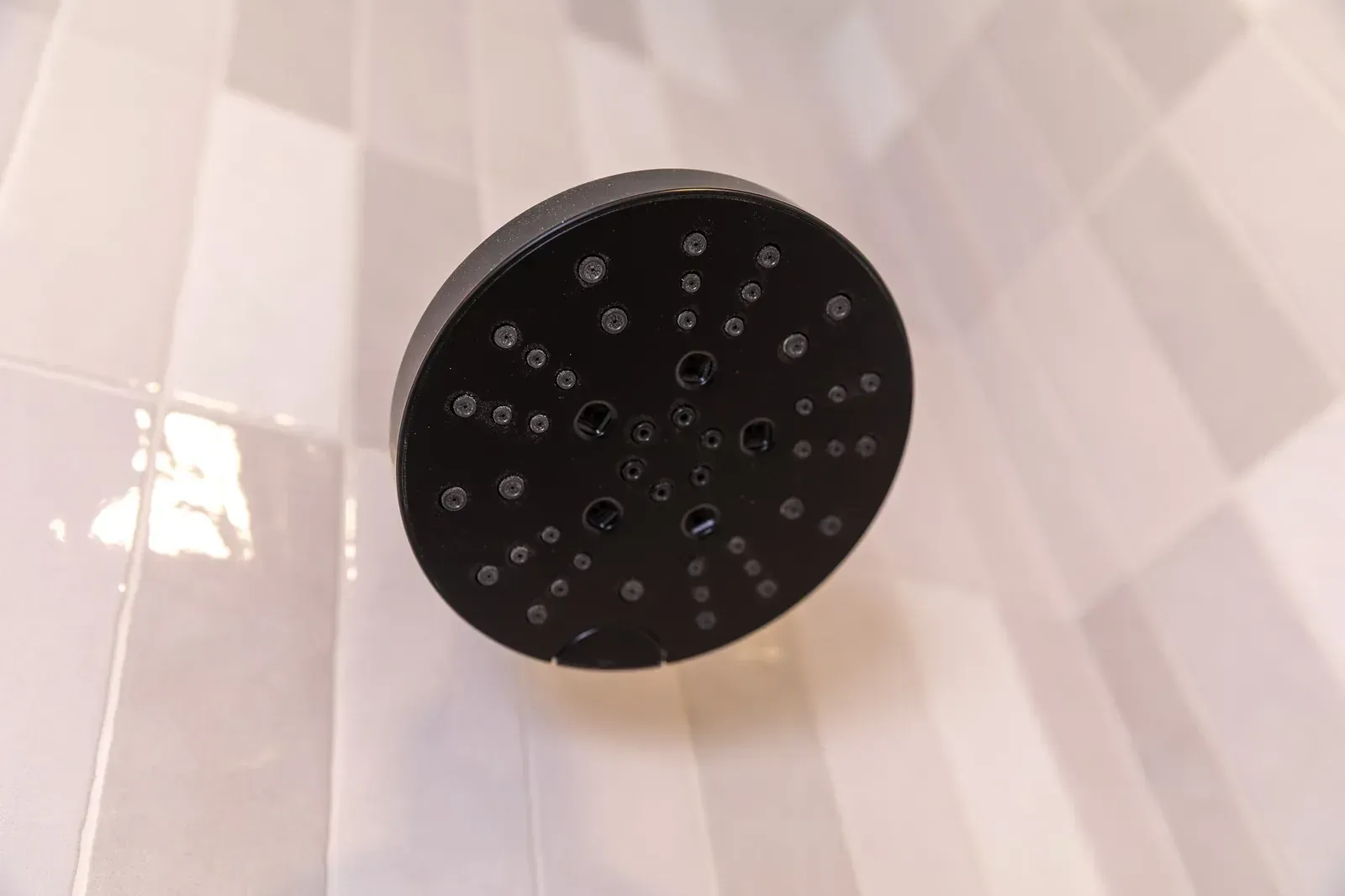 Black showerhead viewed from below against white tiled shower walls.