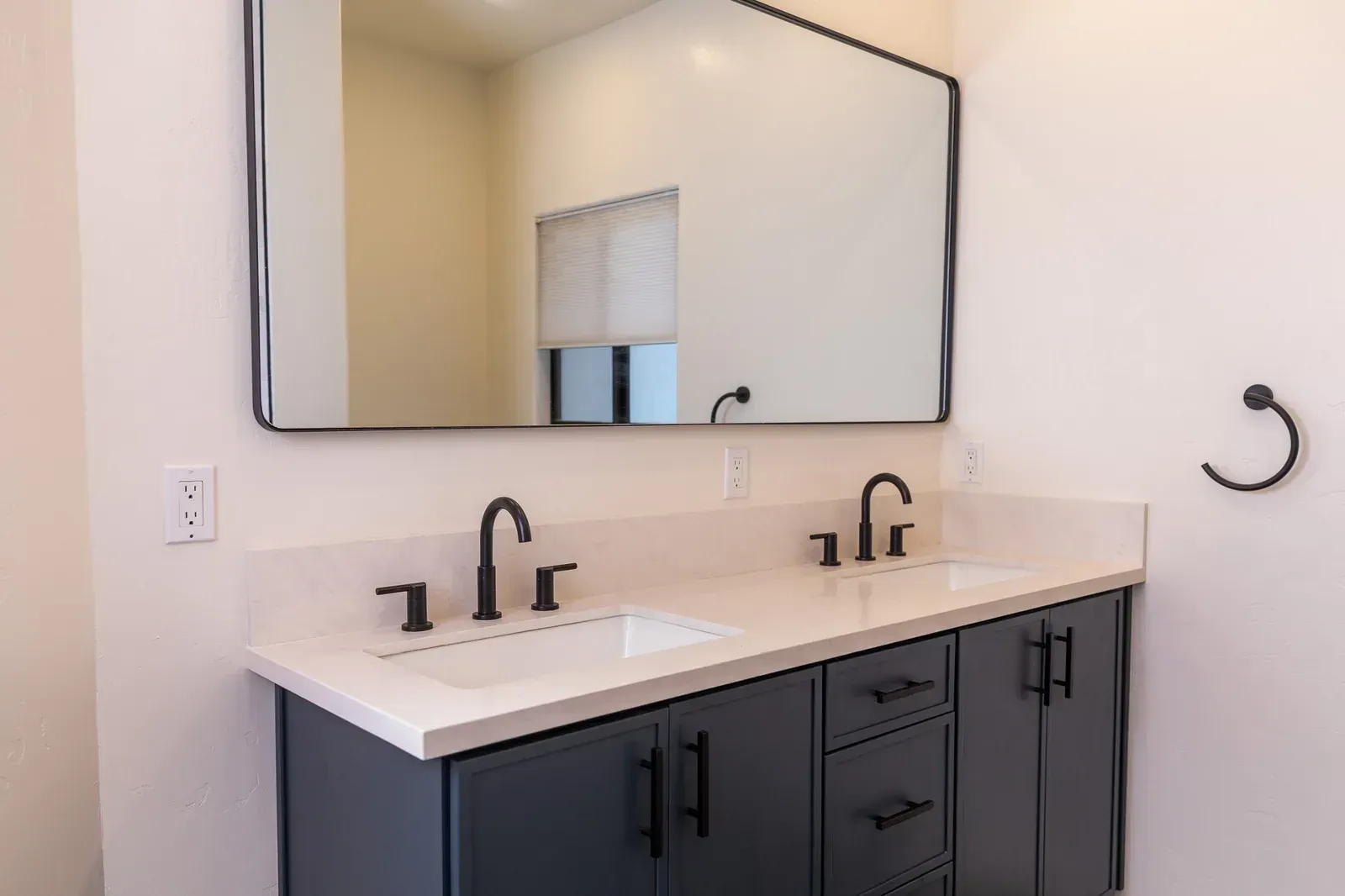 Modern bathroom vanity with double sinks, black fixtures, large mirror, and gray cabinets