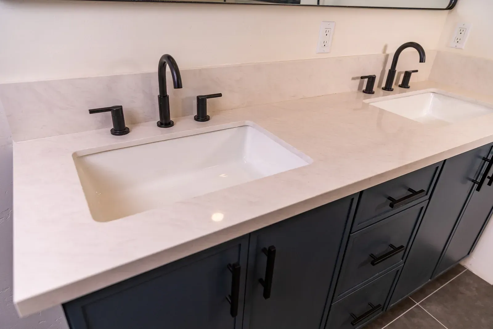 Double-sink bathroom vanity with white countertop and black faucets over dark cabinets