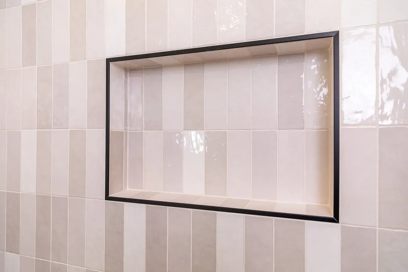 Empty black-framed recessed wall shelf on glossy beige tiled wall.