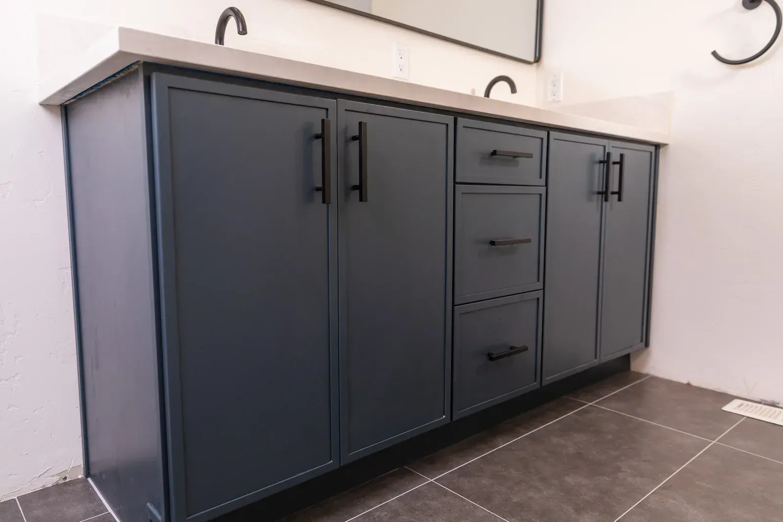 Dark gray bathroom vanity with cabinet doors and drawers against a white wall and tiled floor