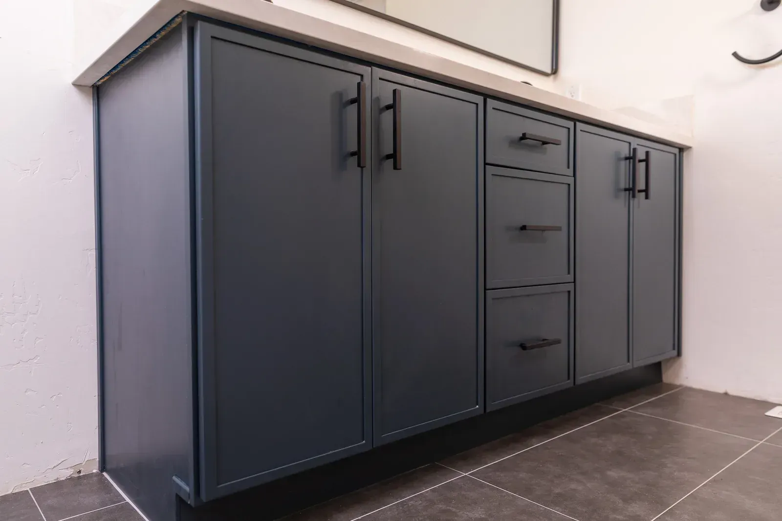 Dark gray kitchen base cabinet with drawers and doors along a tiled wall and floor