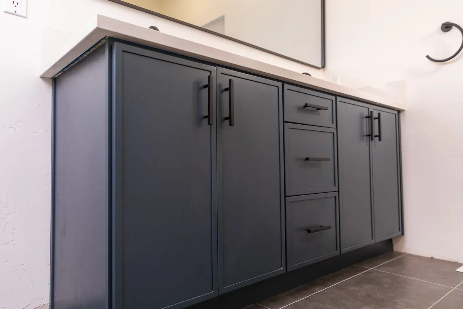 Dark gray bathroom vanity with cabinet doors and drawers beneath a white countertop and mirror.