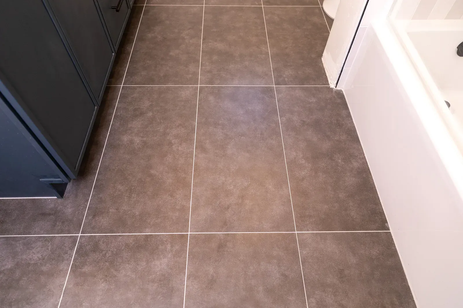 Tiled bathroom floor with dark gray tiles beside a bathtub and cabinet