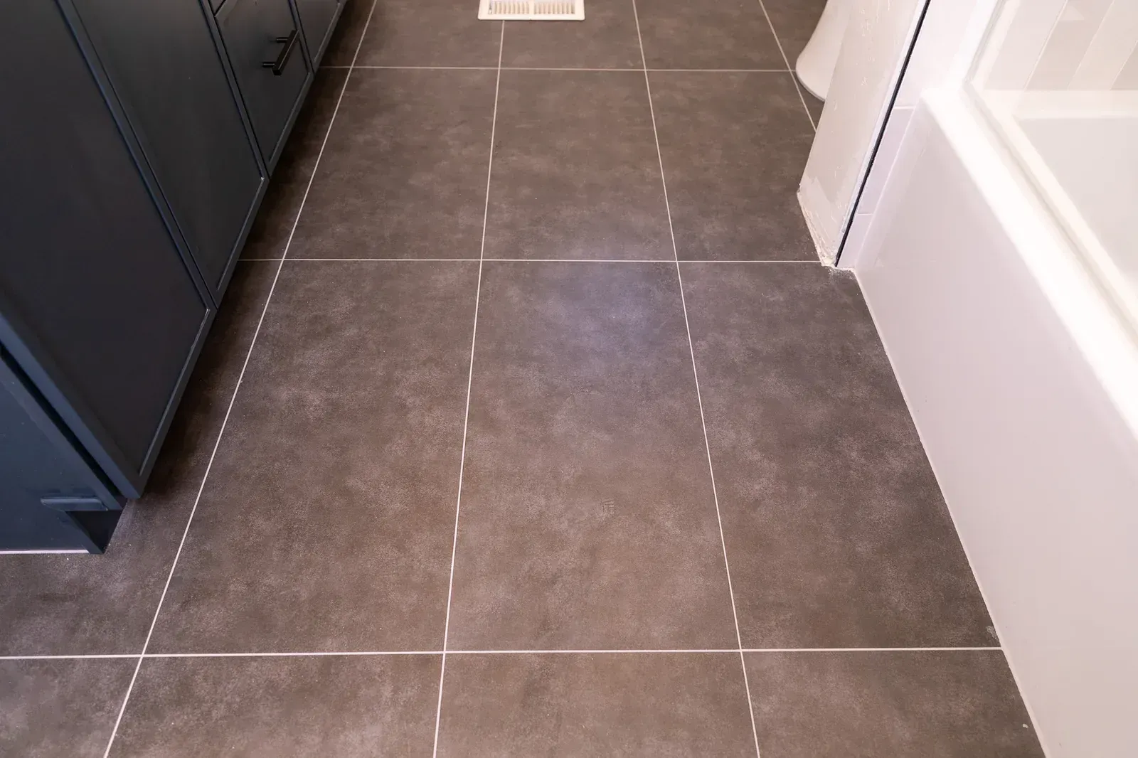 Dark tiled bathroom floor beside a black cabinet and white bathtub wall.