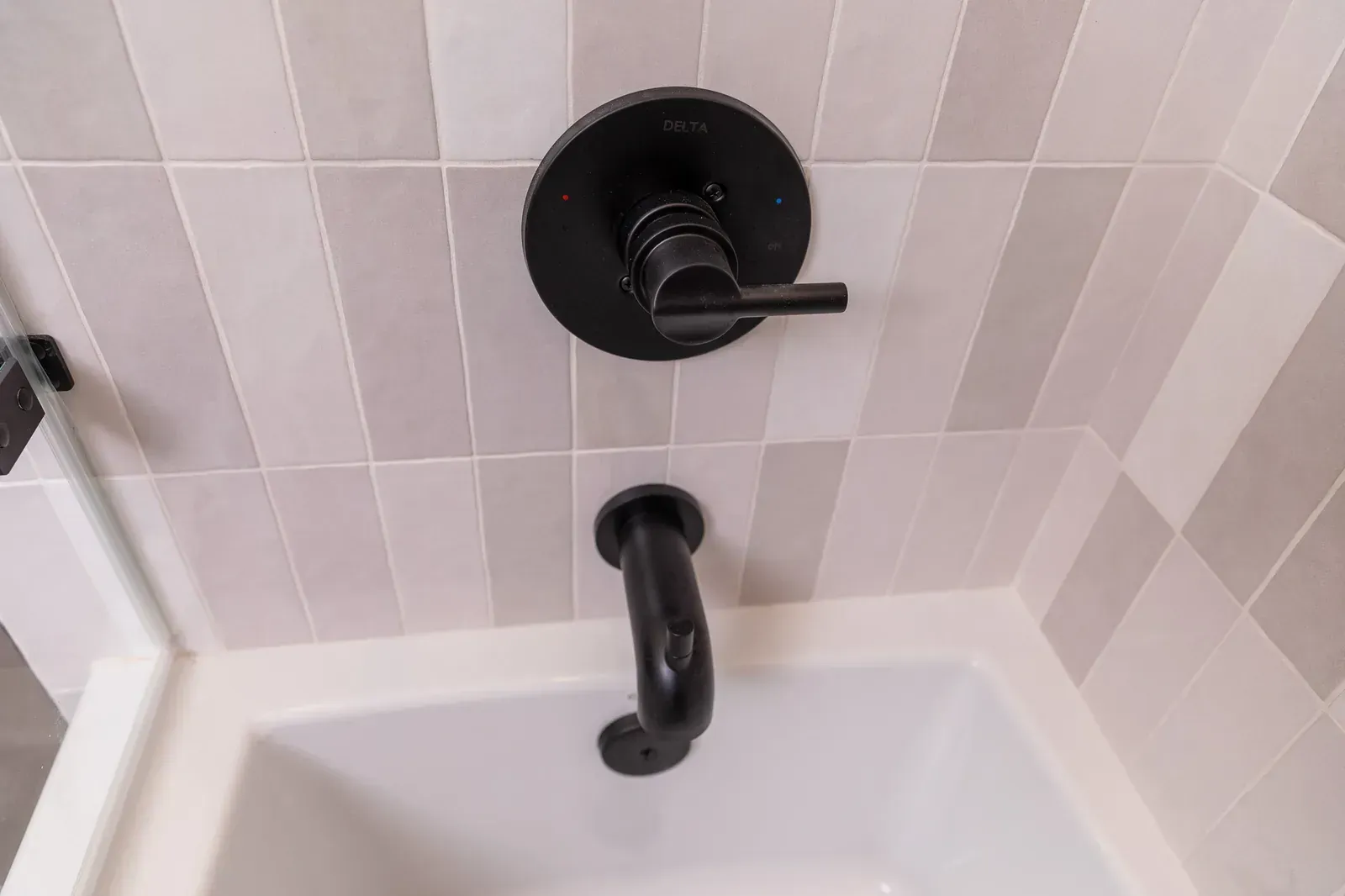 White bathtub corner with black shower handle and wall-mounted faucet controls