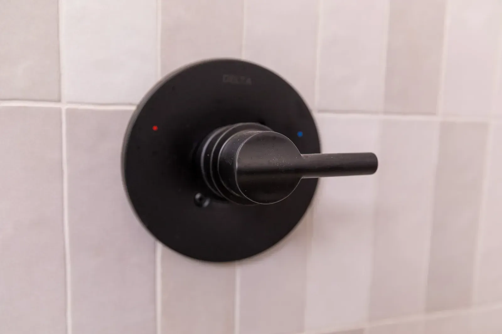 Black shower control knob on light tiled wall