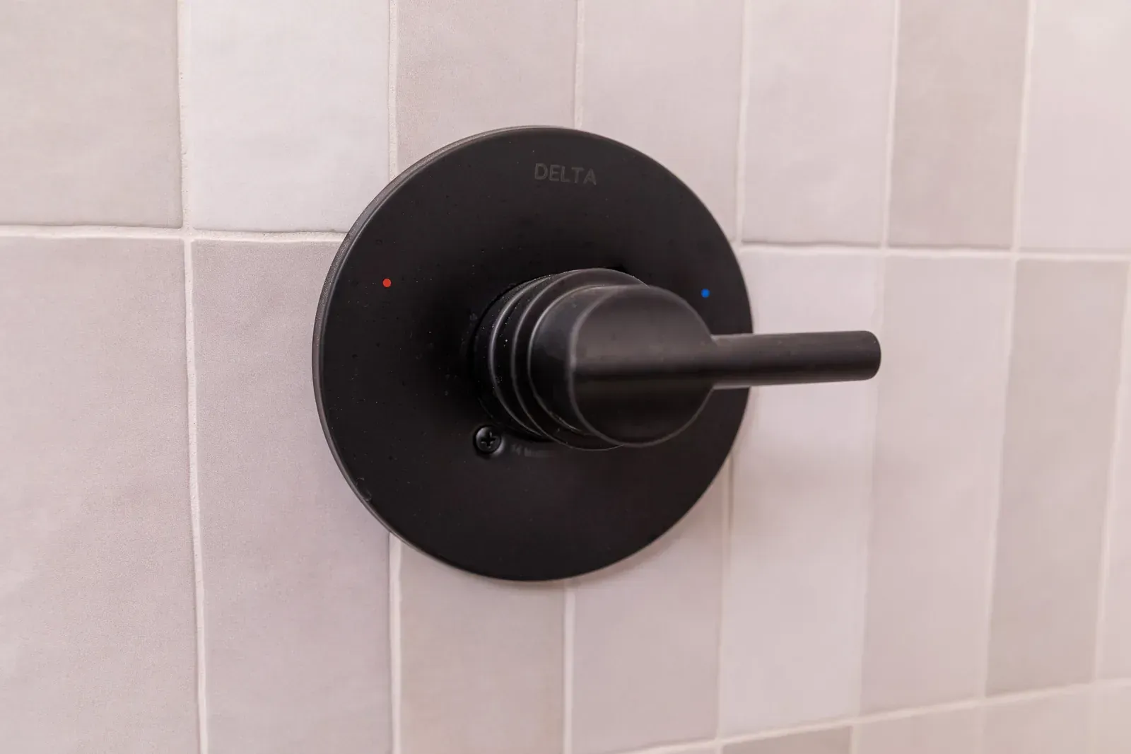 Black shower control knob on a tiled bathroom wall