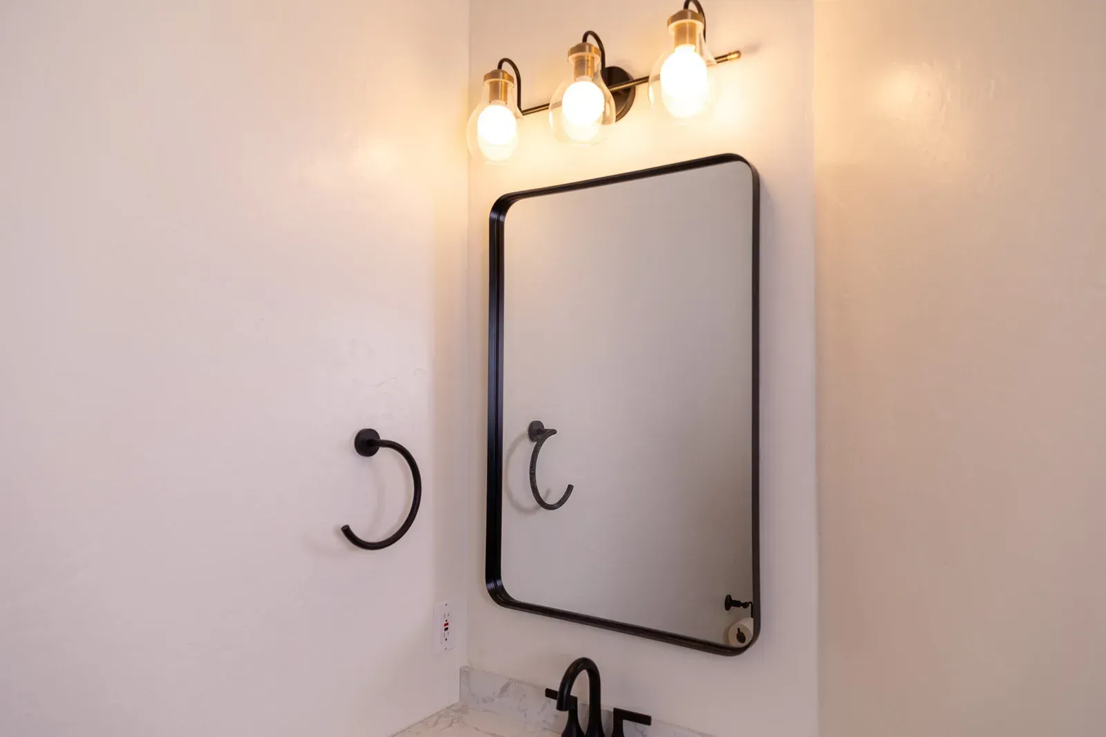 Bathroom vanity mirror with black frame, wall lights, and towel hooks above a sink