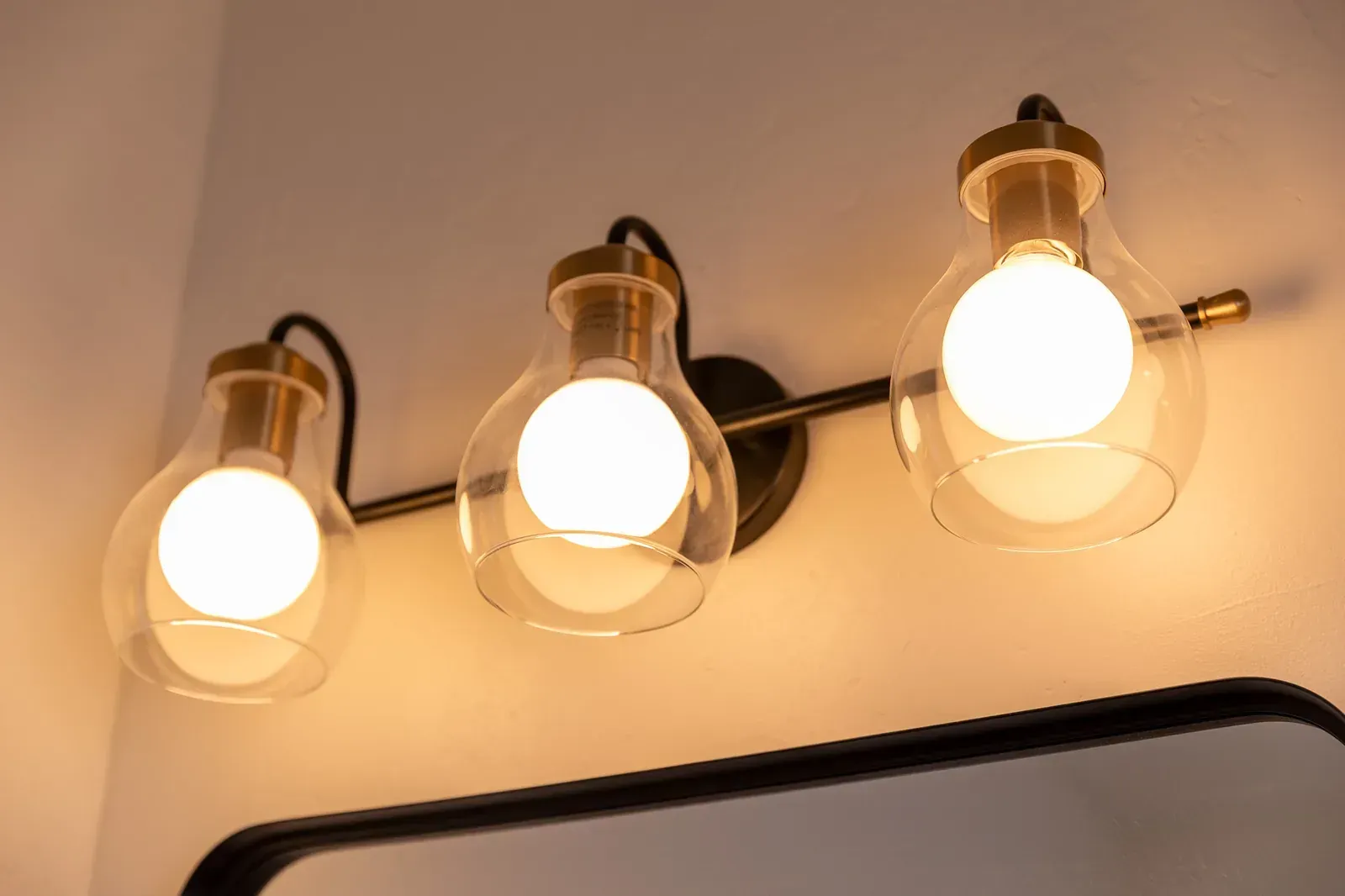 Three glowing vintage bulbs in black sconces on a cream wall above a mirror