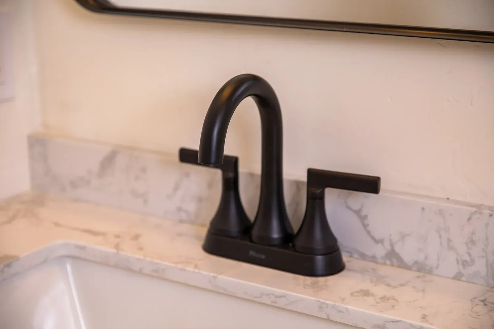 Matte black bathroom faucet on a light marble countertop with sink
