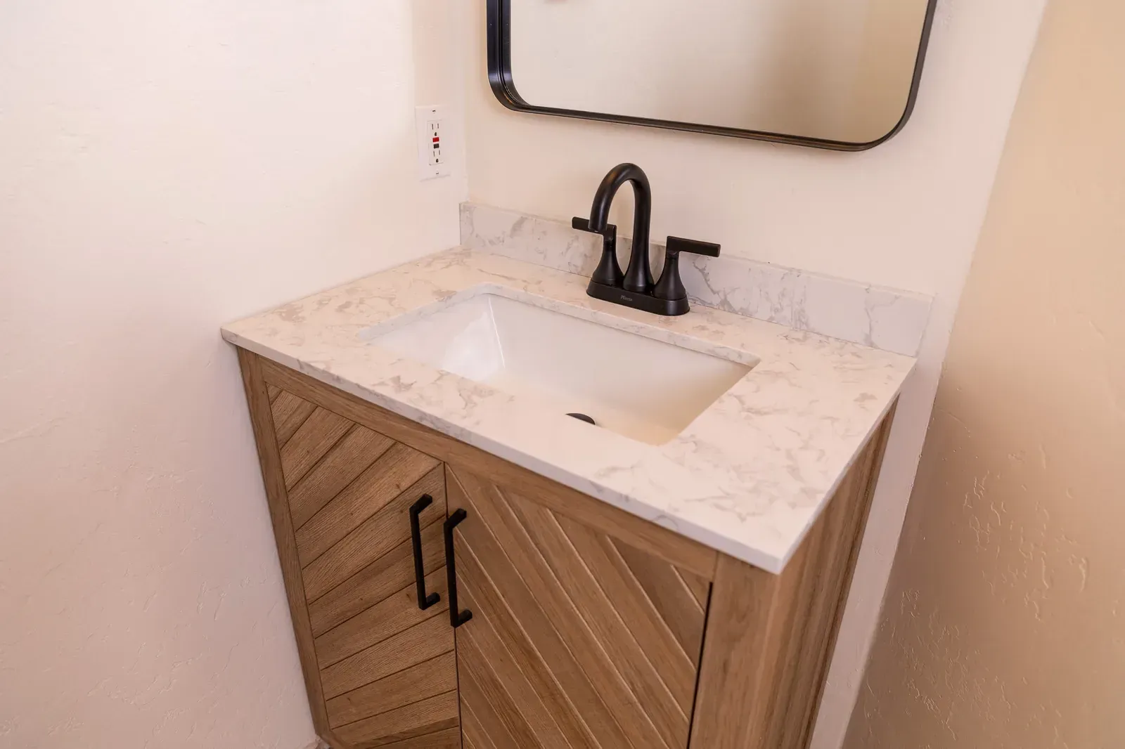 Modern vanity sink with marble countertop, black faucet, and wood cabinet in a small bathroom.