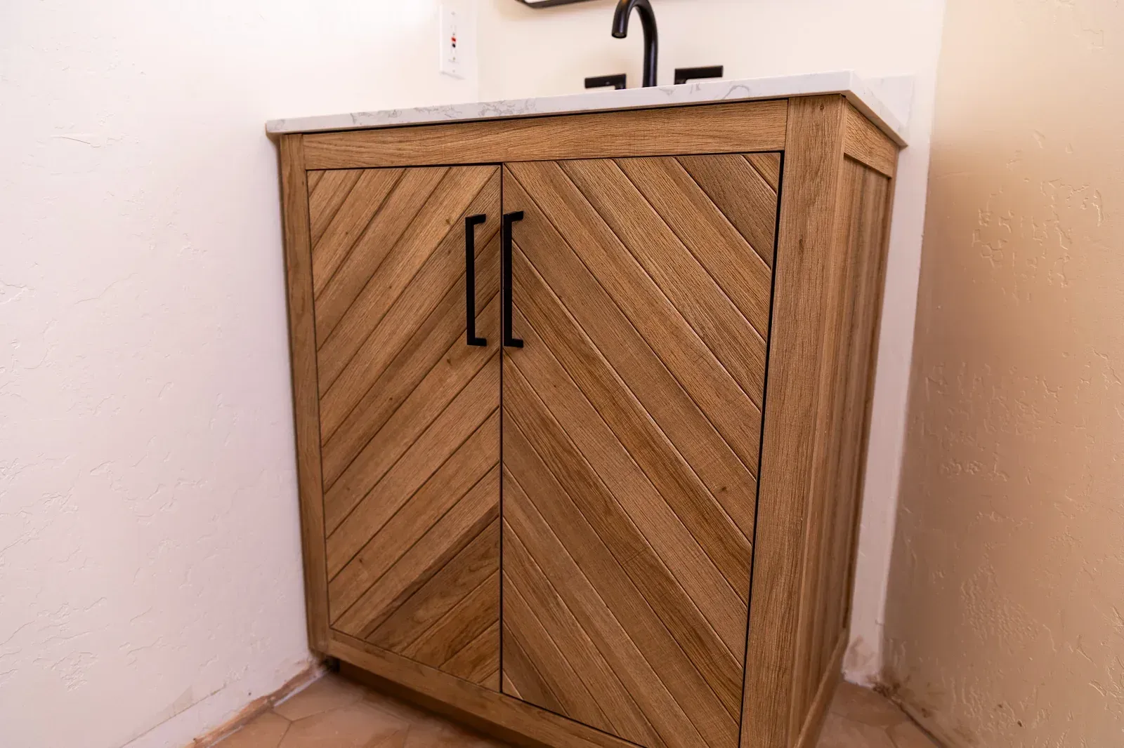 Wooden bathroom vanity cabinet with chevron doors under a sink in a corner alcove
