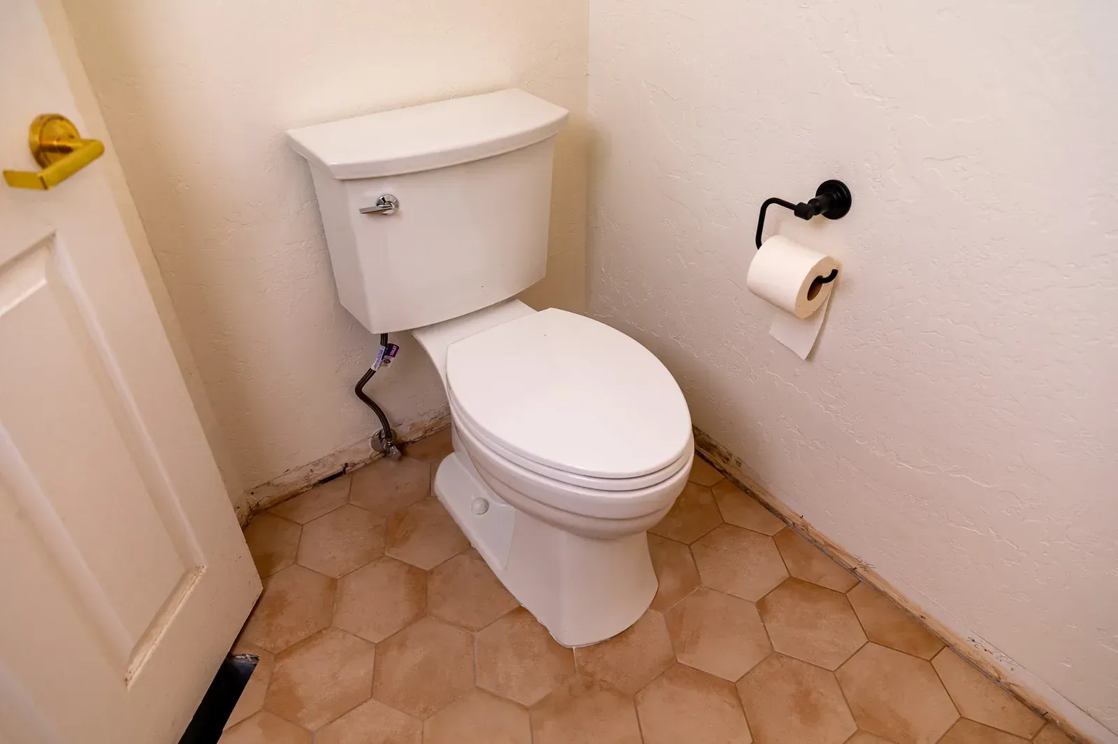 Small bathroom with a white toilet, tan tile floor, and toilet paper holder on the wall.