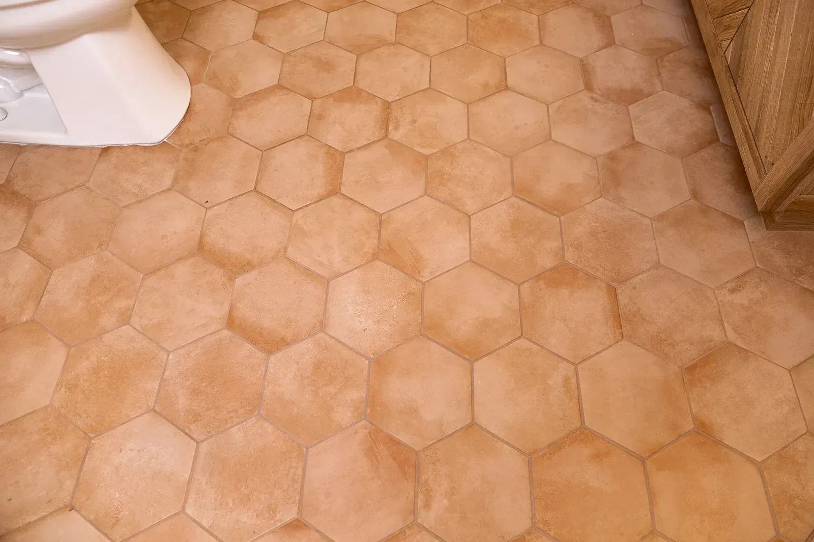 Beige hexagonal tile flooring in a room with a white appliance at left and wicker furniture at right