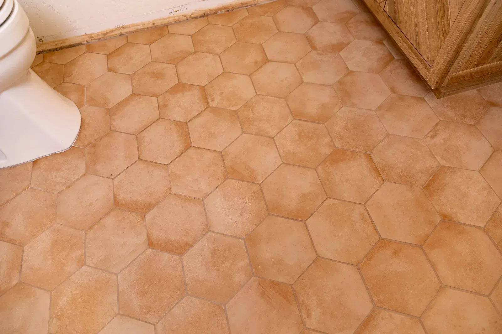 Tan hexagonal tile bathroom floor beside a white toilet and wooden cabinet