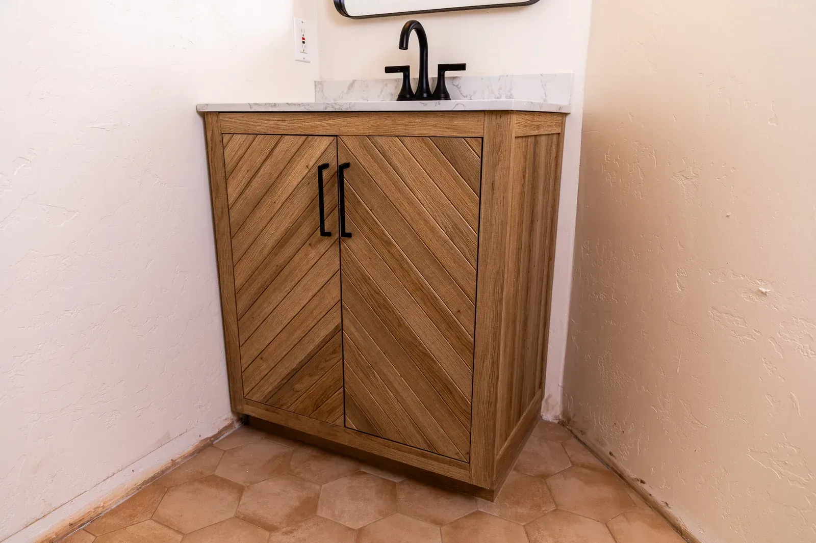 Wooden bathroom vanity with sink and black faucet in a corner against white walls.