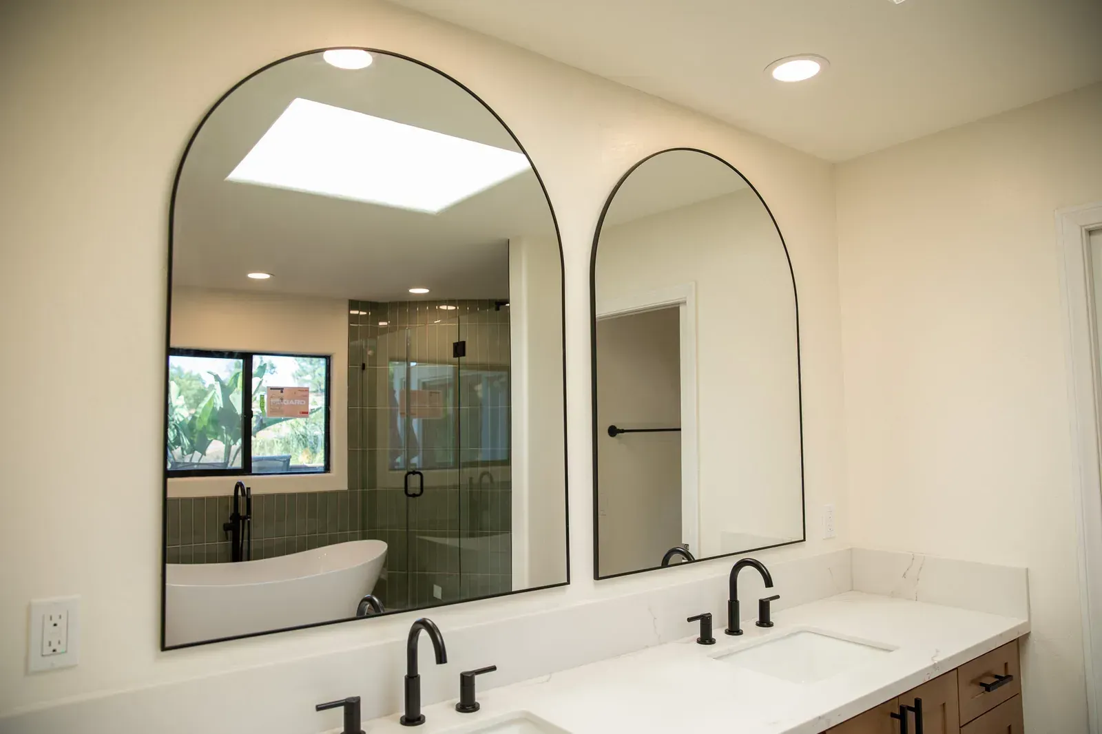 Modern bathroom with arched mirrors, double sink vanity, and glass shower enclosure