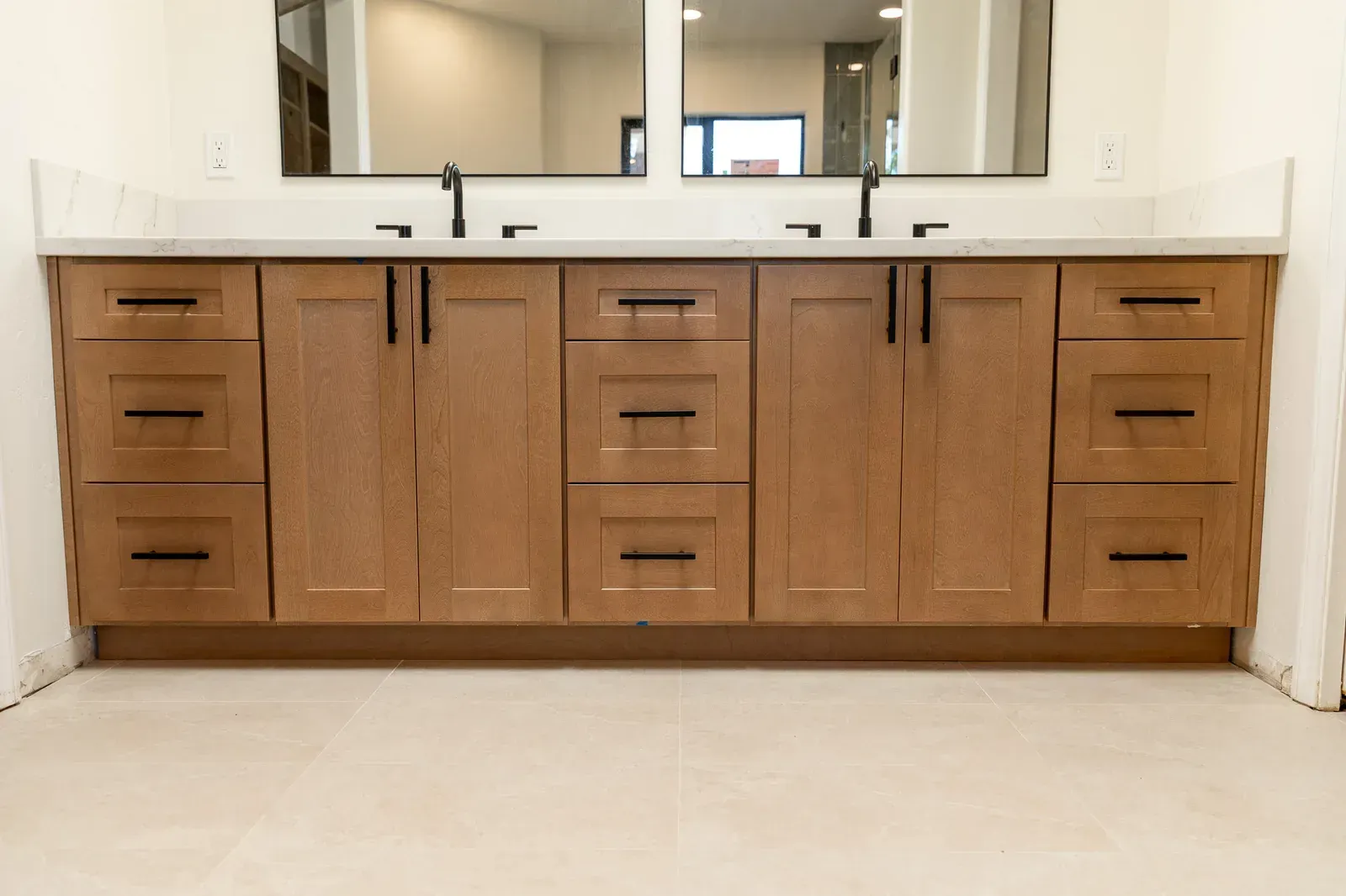 Wood bathroom vanity with double sinks, mirrors, and a light countertop above a beige tile floor