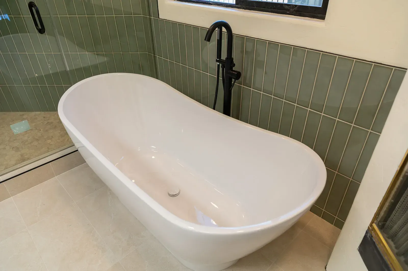 Modern white freestanding bathtub beside a glass shower in a tiled bathroom