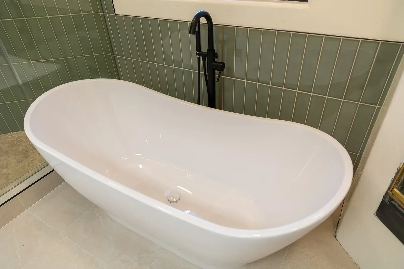White freestanding bathtub with matte black faucet against green tiled bathroom wall