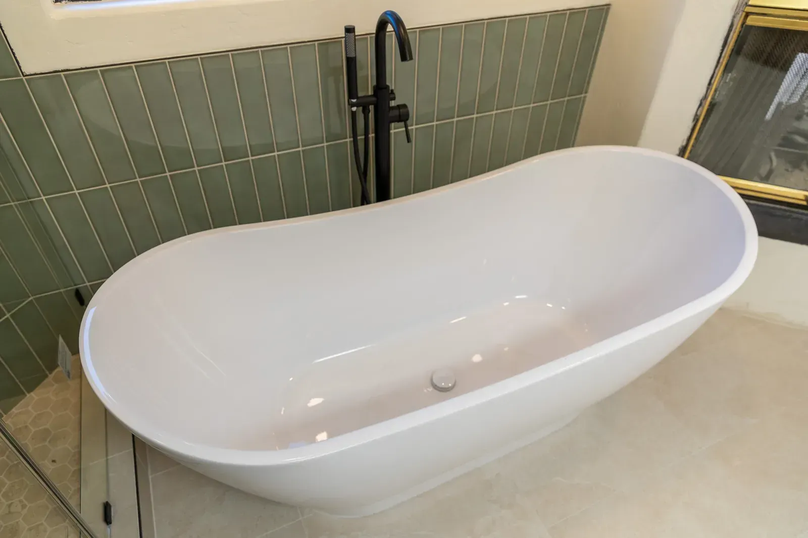Modern white freestanding bathtub with black faucet in a tiled bathroom