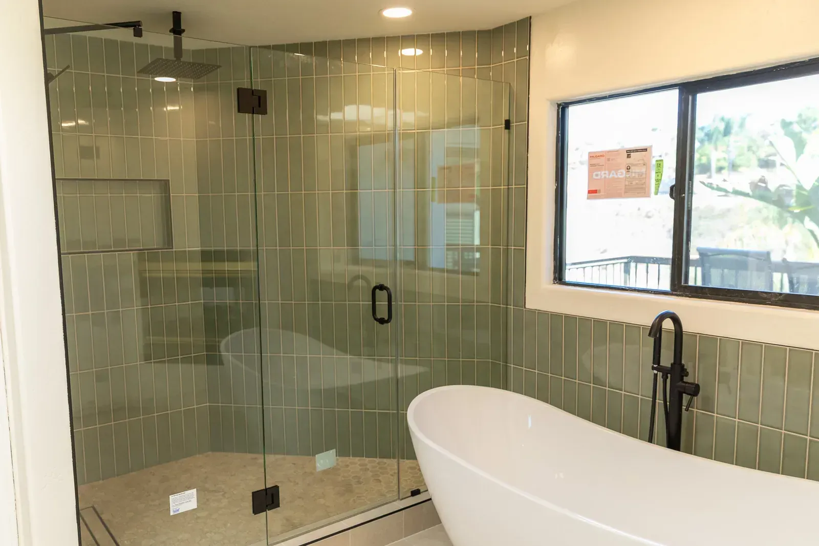 Modern bathroom with glass shower enclosure, freestanding tub, and large window
