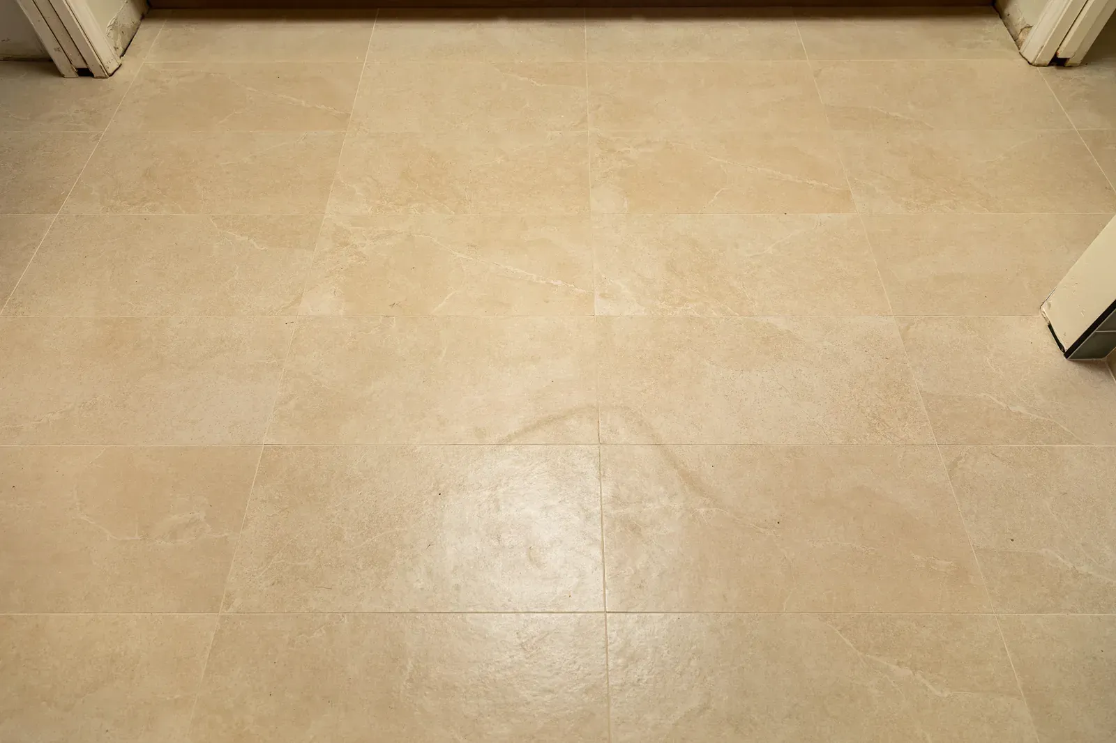 Beige tiled floor with a subtle reflection and white door frames at the top edges