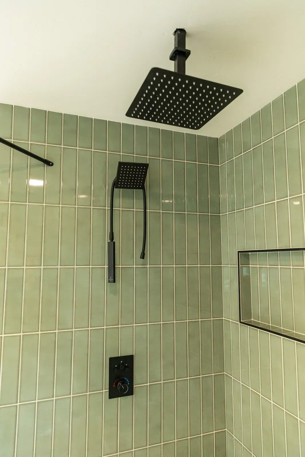 Modern shower with green tile walls and black showerhead