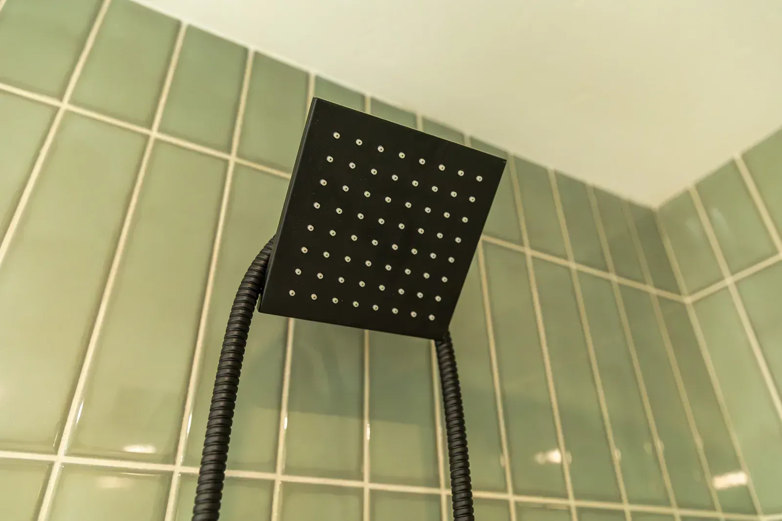 Black square showerhead with hose against green tiled bathroom wall