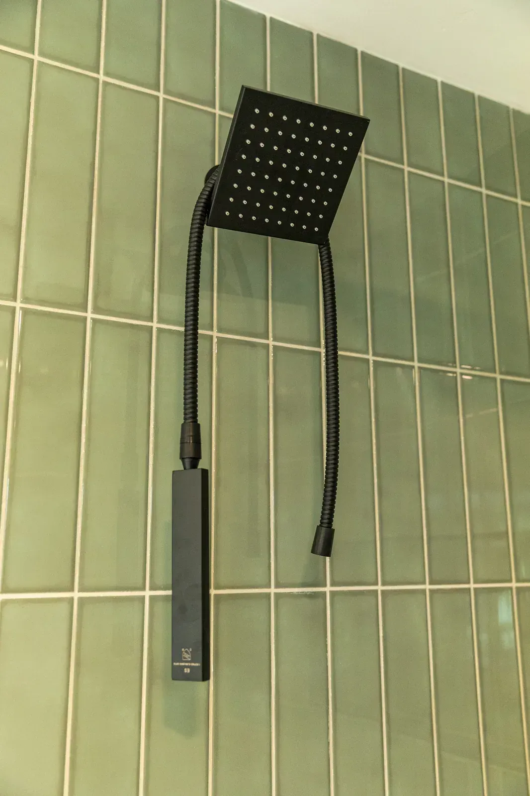 Wall-mounted showerhead with black hose and handheld sprayer on green tiled bathroom wall
