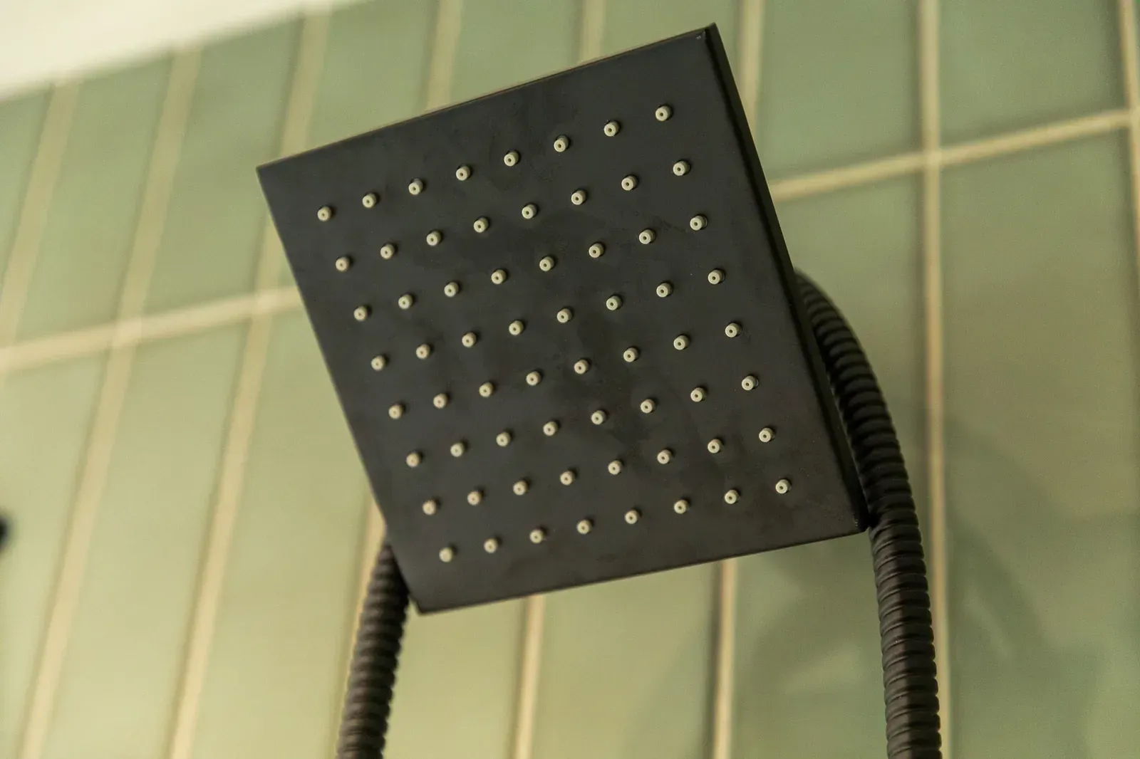 Square black showerhead with water nozzles against a tiled bathroom wall